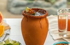 an orange drink in a tall vase next to other fruit and spices on a table