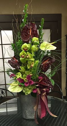 a vase filled with green and purple flowers on top of a glass table next to a window