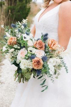 a bride holding a bouquet of flowers in her hands and smiling at the camera while standing on a gravel road