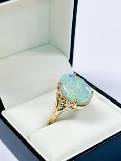 This remarkable gold ring features a large opal with vibrant flashes of green, blue, and yellow, creating a mesmerizing display of color. The bold opal is securely set in a beautifully crafted 9ct gold band, adorned with delicate detailing and brilliant cut diamond set on each sidemaking this ring a standout piece. Opal weight 5.85ct Diamond weight .03ct Ring size Q Approximately weighs 4.8gm Luxury Artisan Opal Ring For Gift, Luxury Gold Opal Ring With Diamond Accents, Diamond Set, Opal Ring, Blue And Yellow, Gold Band, Opal Rings, Brilliant Cut Diamond, Rings Statement