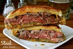 a roast beef sandwich cut in half on a white plate with mustard and cheese over it