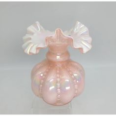 a pink glass vase sitting on top of a clear base with a white bow around it's neck