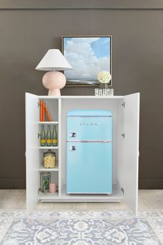 a blue refrigerator sitting inside of a cabinet next to a lamp and pictures on the wall