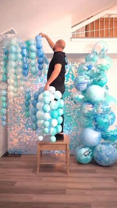 a man standing on a stool in front of blue and white balloons hanging from the ceiling