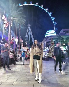 a woman is walking down the street in front of a ferris wheel and christmas lights