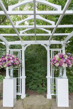 two vases filled with flowers under a white arbor