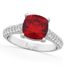 a red cushion cut ring with diamonds on the band and side stones in white gold