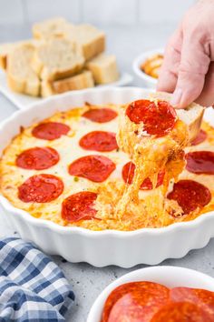 a person is lifting a slice of pizza from a casserole dish with cheese and pepperoni