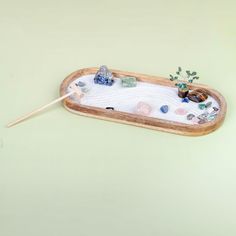 a wooden tray with rocks and plants in it on a green surface, next to a stick