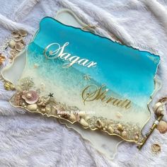 a glass plate with the name sagar and shells on it, sitting on a white blanket