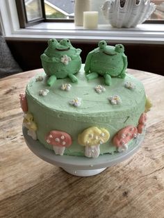 there is a cake with green frosting and two little frogs on top of it