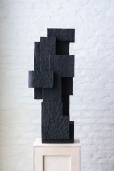 a black sculpture sitting on top of a wooden block in front of a white brick wall