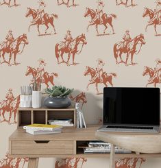 a laptop computer sitting on top of a wooden desk next to a wall with horses