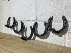 three black horseshoes are hanging on the wall next to a wooden table and white brick wall