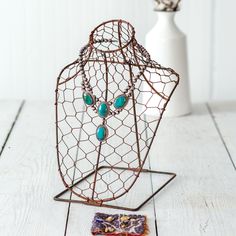 a wire mannequin with turquoise beads on it next to a small piece of fabric