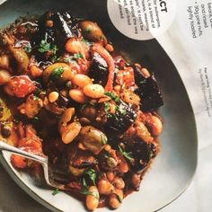 a white plate topped with beans and vegetables on top of a table next to a newspaper