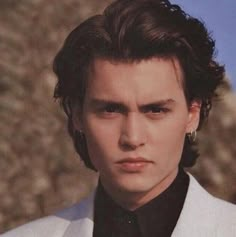 a young man in a white suit and black tie looking at the camera with an intense look on his face