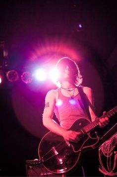 a woman playing guitar in front of purple light