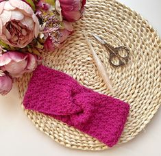 a pink knitted bow tie sitting on top of a woven basket next to flowers