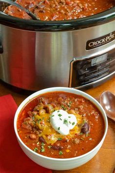 a bowl of chili next to a crock pot on top of a wooden table