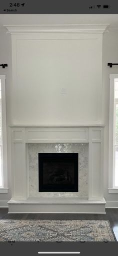 an empty living room with a fireplace and two windows in the wall, along with a rug on the floor