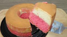 a pink and white cake on a black plate with a slice taken out of it