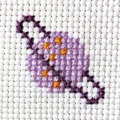 a cross stitch pattern with a purple coffee cup on it's side and an orange dot in the middle