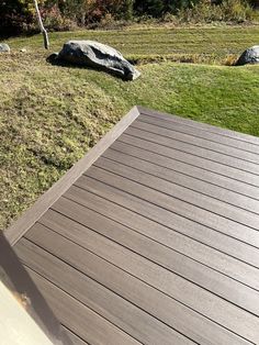 a wooden deck in the middle of a grassy area with rocks and trees behind it