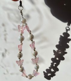 a pair of pink and white beads hanging from a hook on a chain with butterfly charms