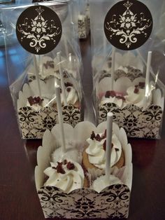 three cupcakes with white frosting and chocolate decorations on them in clear plastic bags