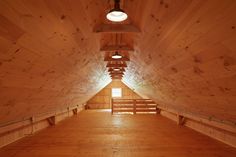 an empty room with wooden walls and beams on the ceiling is lit by a light fixture