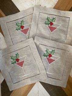 four christmas cocktail napkins with holly on them sitting on a wooden table top next to each other