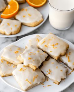 iced orange shortbreads with icing and orange zest on plates next to a glass of milk