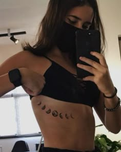 a woman wearing a black bra with phases drawn on her stomach and holding a cell phone