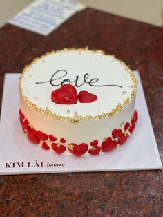 a white cake with red hearts on it and the word love spelled in gold lettering