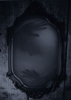 an old fashioned mirror hanging on the side of a wooden wall in black and white