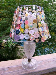 a lamp made out of buttons sitting on top of a wooden table next to trees