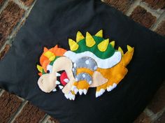 a black pillow with an embroidered dragon on it's back and yellow, orange, and green accents