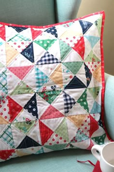 a colorful pillow sitting on top of a blue chair next to a cup and saucer