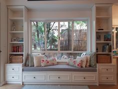 a window seat with pillows on it in front of a bookshelf and shelves