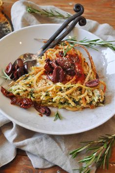 a plate with spaghetti and olives on it, next to two serving utensils