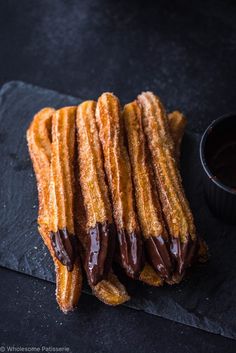 churros with chocolate sauce and dipping sauce on black slate platter next to small bowl