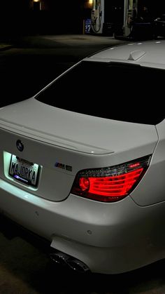 the back end of a silver car parked in a parking lot at night with its lights on