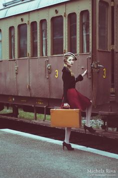 a woman is standing on the train platform with her suitcase