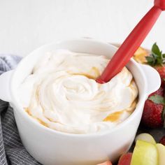 a white bowl filled with whipped cream next to sliced apples and strawberries