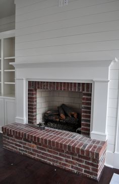 an empty living room with a brick fireplace and built in bookcases on either side