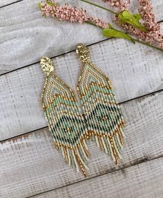 a pair of beaded earrings sitting on top of a wooden table next to pink flowers