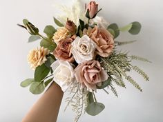 a woman's hand holding a bouquet of flowers and greenery against a white background