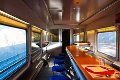 the interior of a train car with tables and chairs on each side, looking out the window