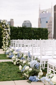 rows of white chairs with blue and white flowers lining the aisle in front of a cityscape